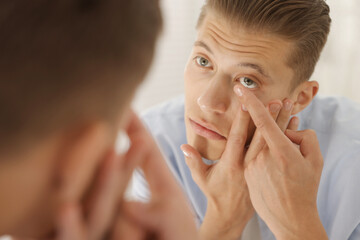 Man putting in contact lens near mirror at home, closeup
