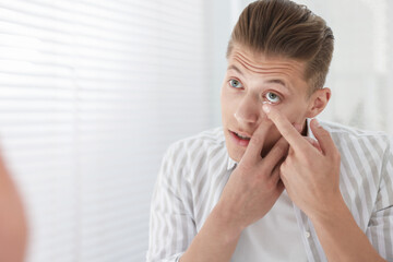 Man putting in contact lens at home. Space for text