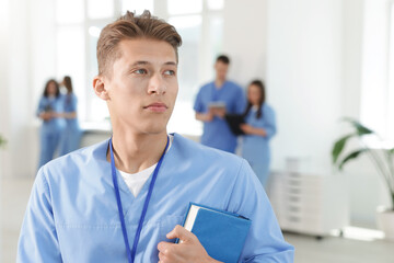 Medical student in uniform with book indoors, selective focus