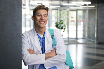 Medical student in uniform with backpack indoors, space for text