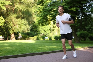 Sporty man with armband running in park, space for text