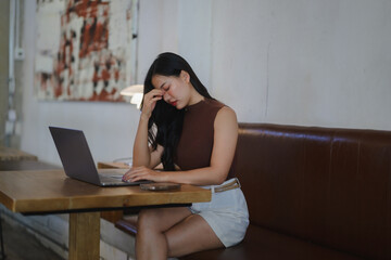 Young asian businesswoman suffering from headache while working on laptop in cafe, feeling tired...