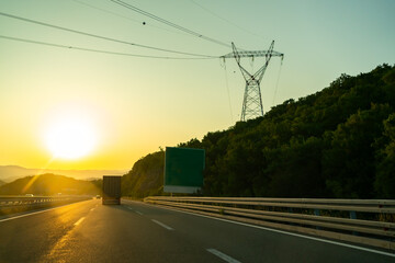 Scenic view of a truck driving on a highway during sunset, with power lines and pylons silhouetted...