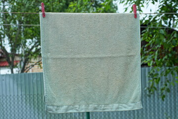 one large clean stylish gray with patterns soft home wet cloth washed towel hanging on a rope with red plastic clothespins during daytime outdoors in summer