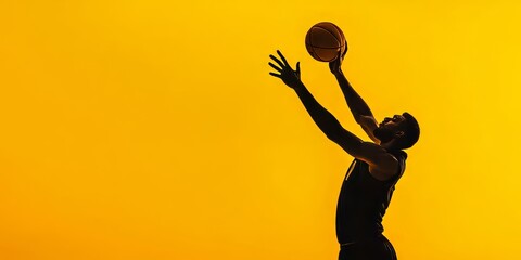 The basketball athlete's silhouette is accentuated by a bold yellow backdrop as he executes a dramatic action shot for his impressive dunking move.