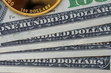 Gold coin with a face value of 100 dollars against the background of a hundred dollar bills