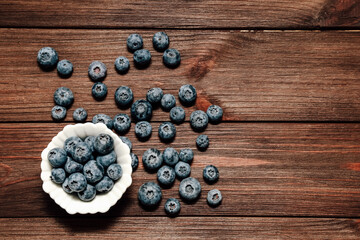 Fresh blueberries scattered beside a bowl on a rustic wooden table