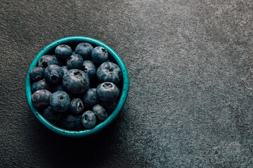 Fresh blueberries in a turquoise bowl on a dark surface for healthy snacking