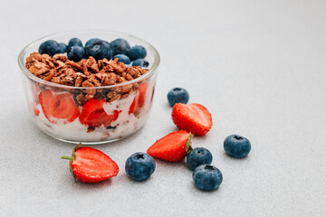 Delicious parfait with strawberries blueberries and granola in a glass bowl on a gray surface