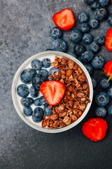 Delicious granola with blueberries and strawberries served in a bowl on a dark surface