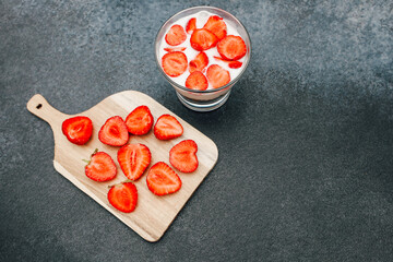 Freshly sliced strawberries with cream served in a glass on a stylish wooden board