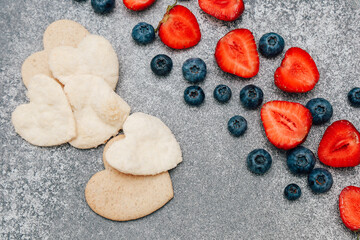 Heart-shaped cookies and fresh strawberries with blueberries on a gray surface
