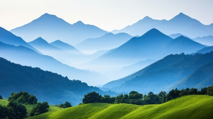 A serene landscape featuring rolling green hills and multiple layers of blue mountain ranges fading into the distance under a clear sky.