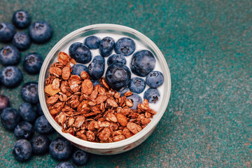 Healthy breakfast bowl with granola and fresh blueberries on green background