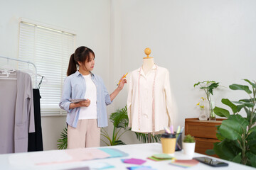 Fototapeta premium Young Asian Female Fashion Designer Creating Clothes on Mannequin in Studio Designing New Collection Trendy Garment Apparel Clothing Boutique Tailor Atelier