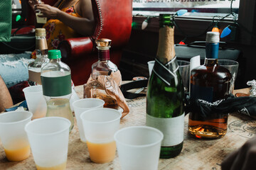 Assorted liquor and champagne bottles with orange juice in plastic cups on wooden table at casual...