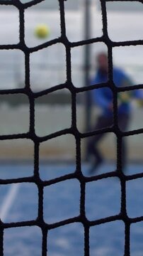 Slowmotion through grid view of paddle tennis man playing on blue court outdoors. One caucasian padle player sportman hitting the ball. Racquet sport game Concept.