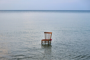 Wooden chair stands in calm, vast ocean, symbolizing solitude and contemplation. Stillness of water...