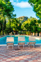 three white desk chairs or chaise lounge with blue swimming pool and hotel green garden on backgeound of vacation summer landscape