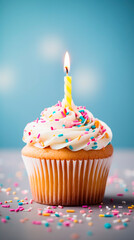A close up of a vanilla cupcake with white frosting and a lit candle on a blue background cake