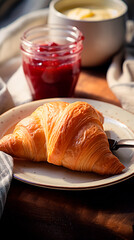 A croissant on a plate with jam and a bowl of cream on a wooden table in soft morning light