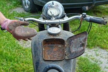 open rusty iron black glove box lid for tools in an old rusty  gasoline closed  tank with steering wheel and headlight in a classic retro heavy broken motorcycle during the day on the street