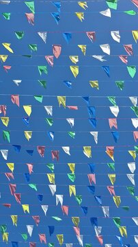 V&aacute;rias bandeirinhas coloridas presas em barbante se movendo com o vento contra o c&eacute;u azul claro.