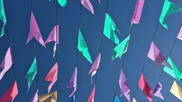 Bandeirinhas festivas penduradas ao ar livre dan&ccedil;ando ao vento com fundo azul.