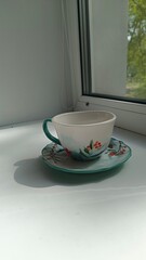 A cup and saucer stands on the windowsill against the background of the window