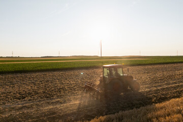 Agricultural tractor is working on the field with wind turbines. Aerial view