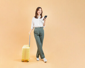 Happy Asian business woman holding smartphone and suitcase isolated on beige color background, travel concept.