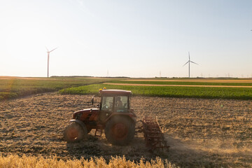 Obraz premium Agricultural tractor is working on the field with wind turbines. Aerial view