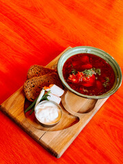 Delicious red soup served with bread and sour cream on a wooden tray