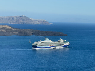 Cruise ship sailing near a rugged island coastline, captured against a wide expanse of vivid blue...
