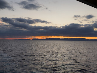 Peaceful ocean view at sunset with dramatic clouds and a glowing orange horizon behind a distant island