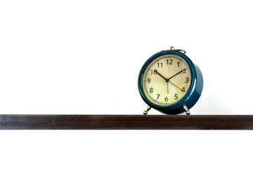 Vintage blue alarm clock displaying time at 10:10 placed on dark wooden shelf with clean white...