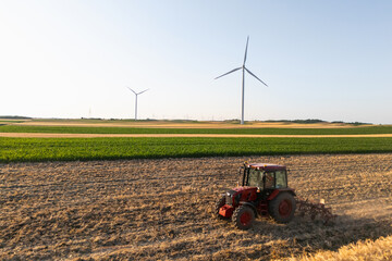 Agricultural tractor is working on the field with wind turbines. Aerial view