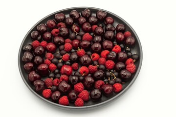 Cherry, raspberry and currant composition on a black plate on a white background - close-up of a berry composition