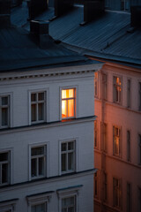 warm glow emanating from small house window at night surrounded by shadows of neighboring buildings