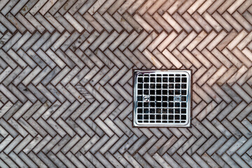 A shiny metal shower drain with diagonal herringbone tiles