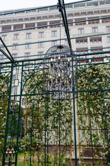 A decorative arch decorated with lush greenery and round illuminated chandeliers.