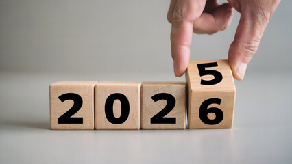 A person s finger is flipping a wooden block from the number six to the number five changing the year from 2026 to 2025