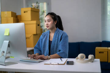 Young Asian woman entrepreneur working on computer in home office managing her business, selling online
