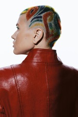 Woman with colorful shaved hair and artistic patterns wearing a red leather jacket against white...
