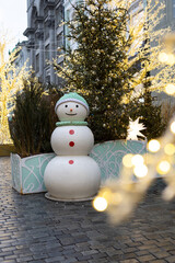 A cheerful snowman stands in a festive urban setting. Decorated with elegant Christmas trees and twinkling lights, creating the atmosphere of a winter holiday.