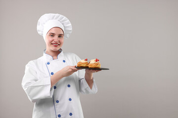 Confectioner in uniform holding delicious profiteroles on light grey background, space for text