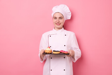 Confectioner in uniform holding different delicious desserts on pink background