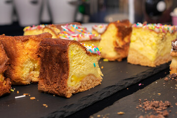 Plate of assorted desserts with colorful sprinkles on top. The desserts are arranged in a way that they look like they are cut into small pieces. The plate is placed on a black surface.