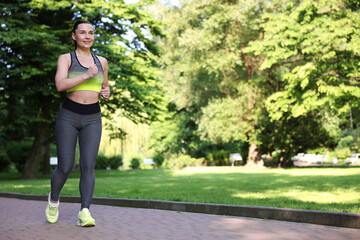 Sporty woman running in park, space for text