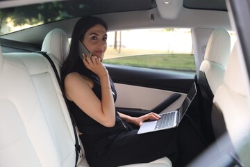 Woman with laptop talking on smartphone in modern car, view from outside